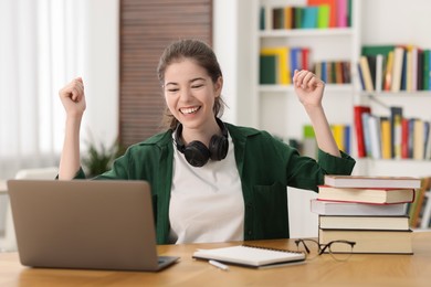 Photo of Preparing for exam. Cheerful student with laptop at table indoors