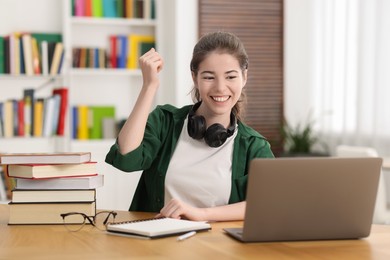 Photo of Preparing for exam. Cheerful student with laptop at table indoors