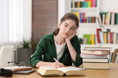 Photo of Preparing for exam. Tired student with books at table indoors