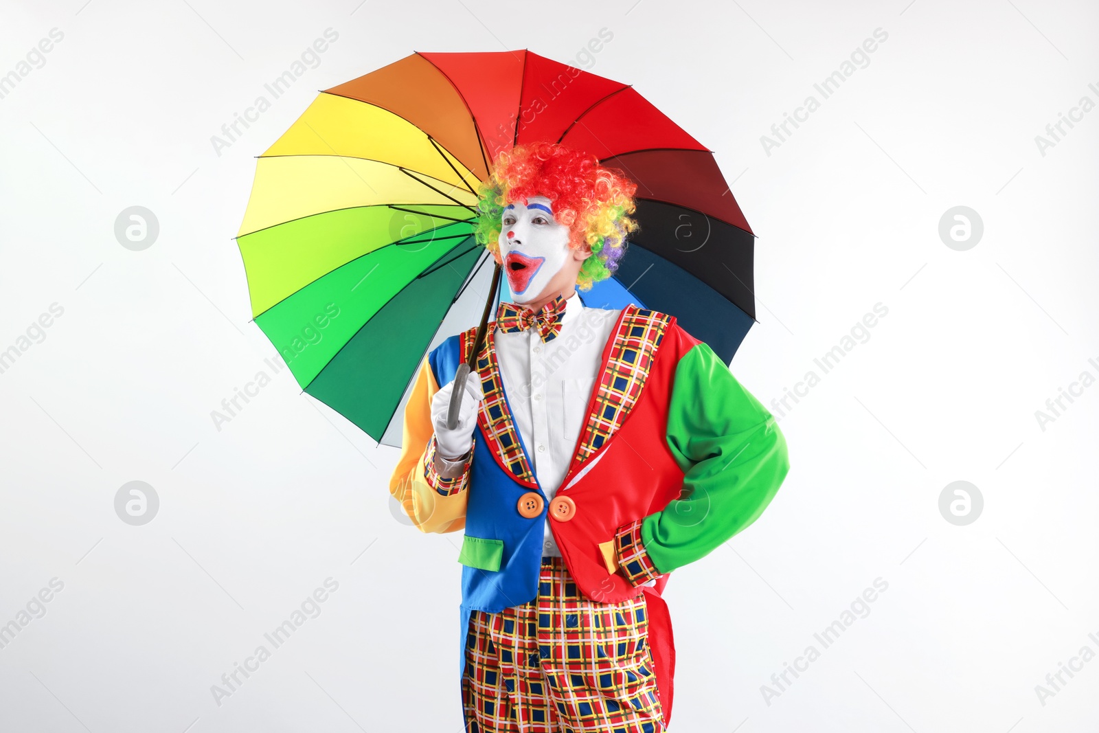 Photo of Emotional clown with colorful umbrella on light background, space for text