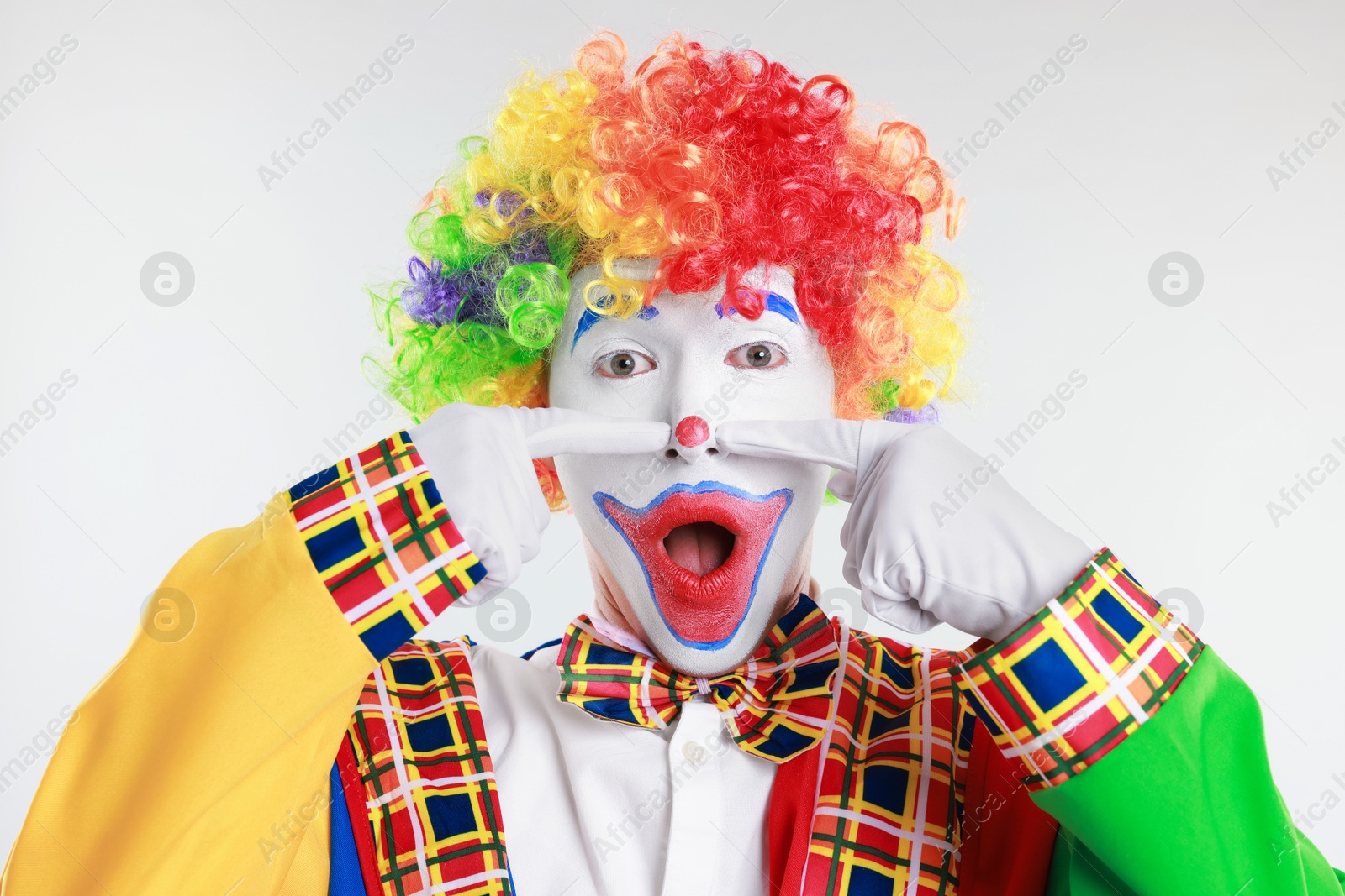 Photo of Emotional clown touching his nose on light background