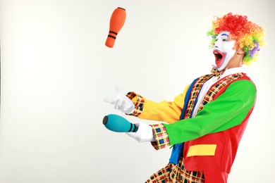 Photo of Clown juggling clubs on light background, space for text