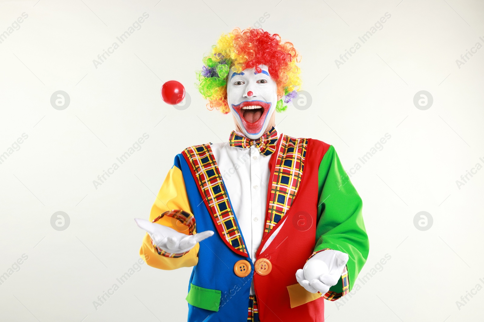 Photo of Funny clown juggling balls on light background