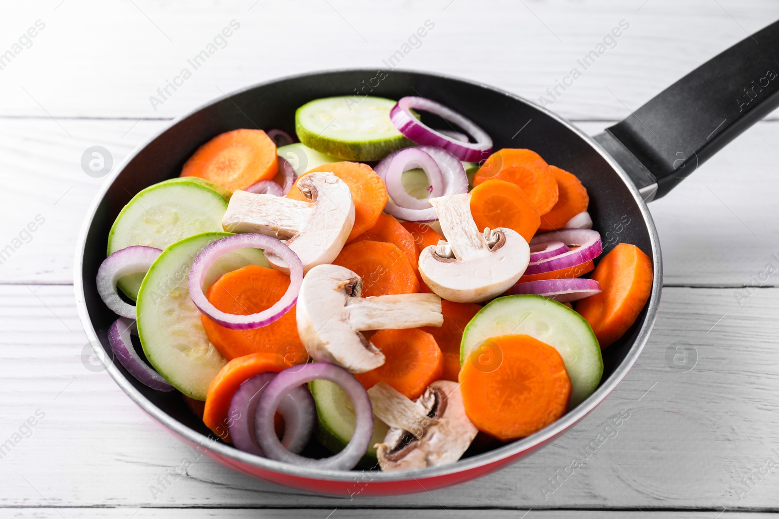 Photo of Frying pan with mix of fresh vegetables and mushrooms on white wooden table, closeup