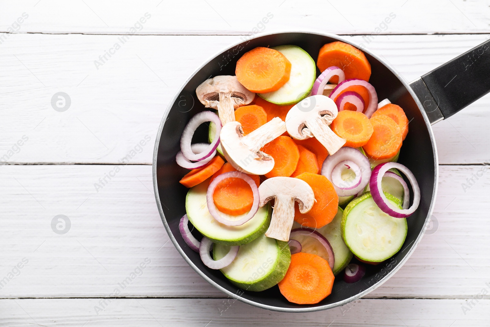 Photo of Frying pan with mix of fresh vegetables and mushrooms on white wooden table, top view