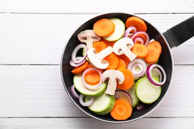 Photo of Frying pan with mix of fresh vegetables and mushrooms on white wooden table, top view