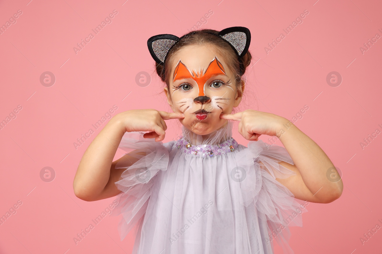 Photo of Cute girl with painted face and ears as cat on pink background