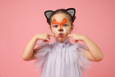 Photo of Cute girl with painted face and ears as cat on pink background