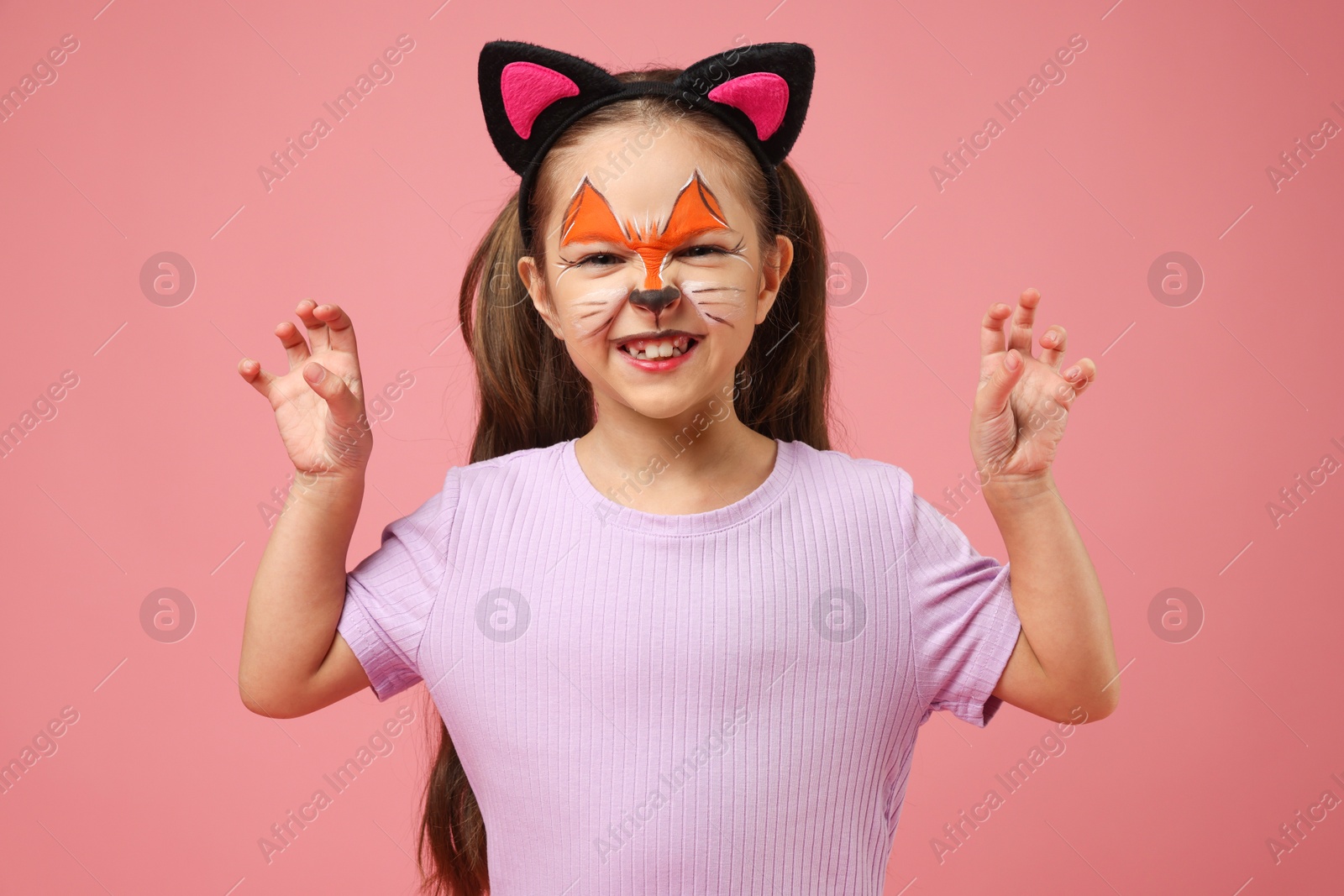 Photo of Cute girl with painted face and ears as cat on pink background