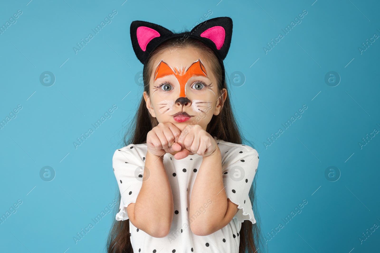 Photo of Cute girl with painted face and ears as cat on light blue background