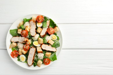 Tasty Caesar salad with chicken and tomatoes on white wooden table, top view. Space for text