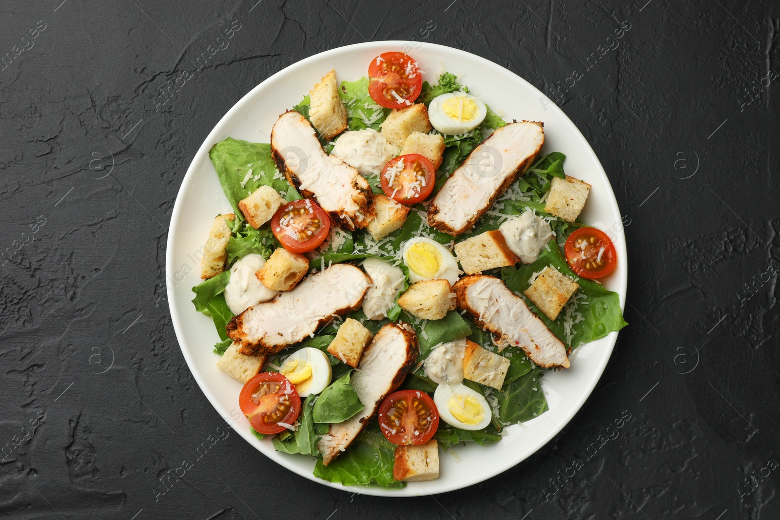 Photo of Tasty Caesar salad with chicken and tomatoes on black table, top view