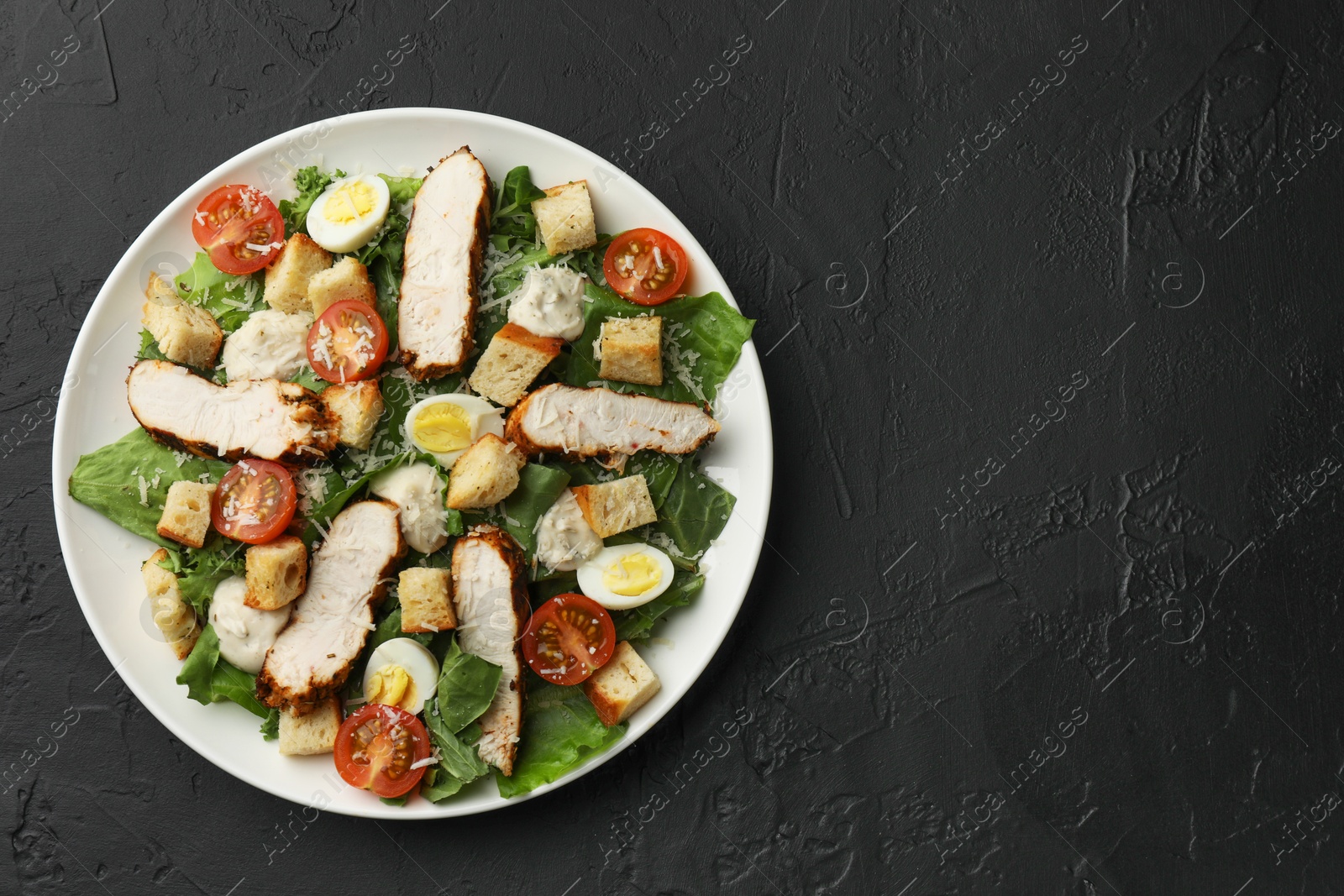 Photo of Tasty Caesar salad with chicken and tomatoes on black table, top view. Space for text