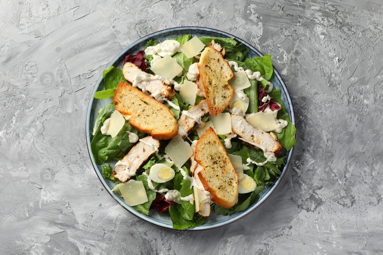 Photo of Tasty Caesar salad with chicken on gray textured table, top view