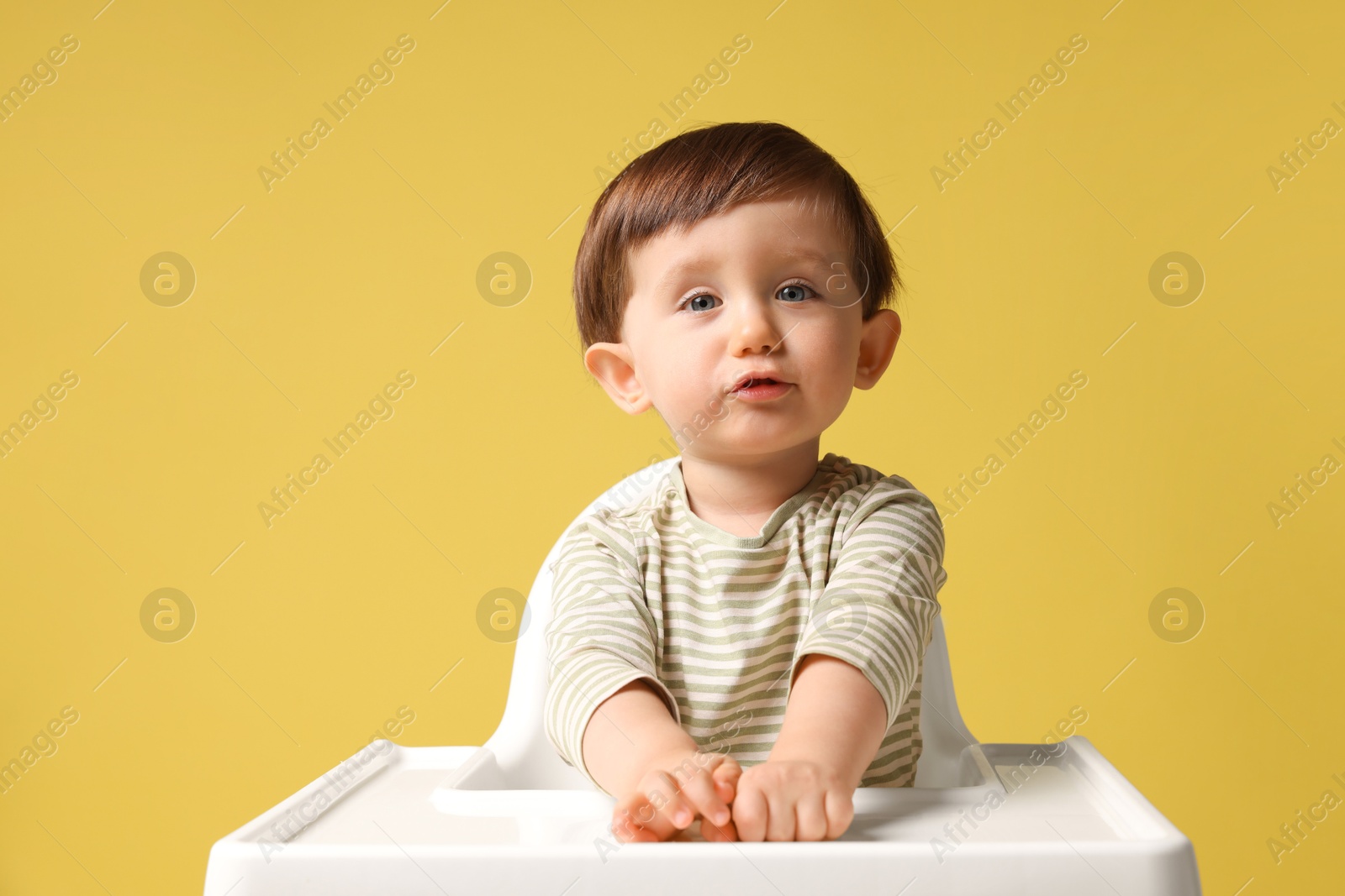 Photo of Cute little kid sitting in high chair on yellow background