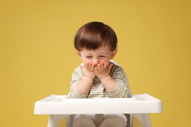 Photo of Cute little kid sitting in high chair on yellow background