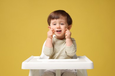 Photo of Cute little kid sitting in high chair on yellow background