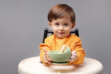 Photo of Cute little kid eating healthy baby food from bowl in high chair on light grey background