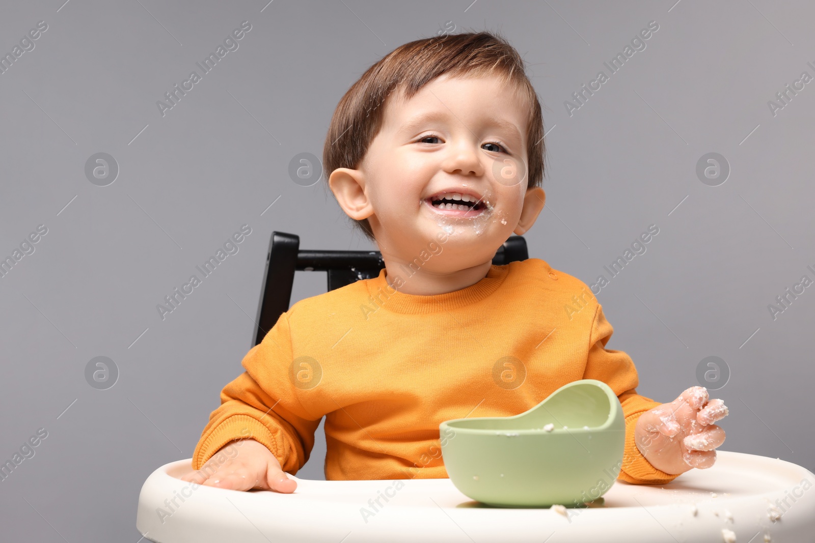 Photo of Cute little kid eating healthy baby food from bowl in high chair on light grey background