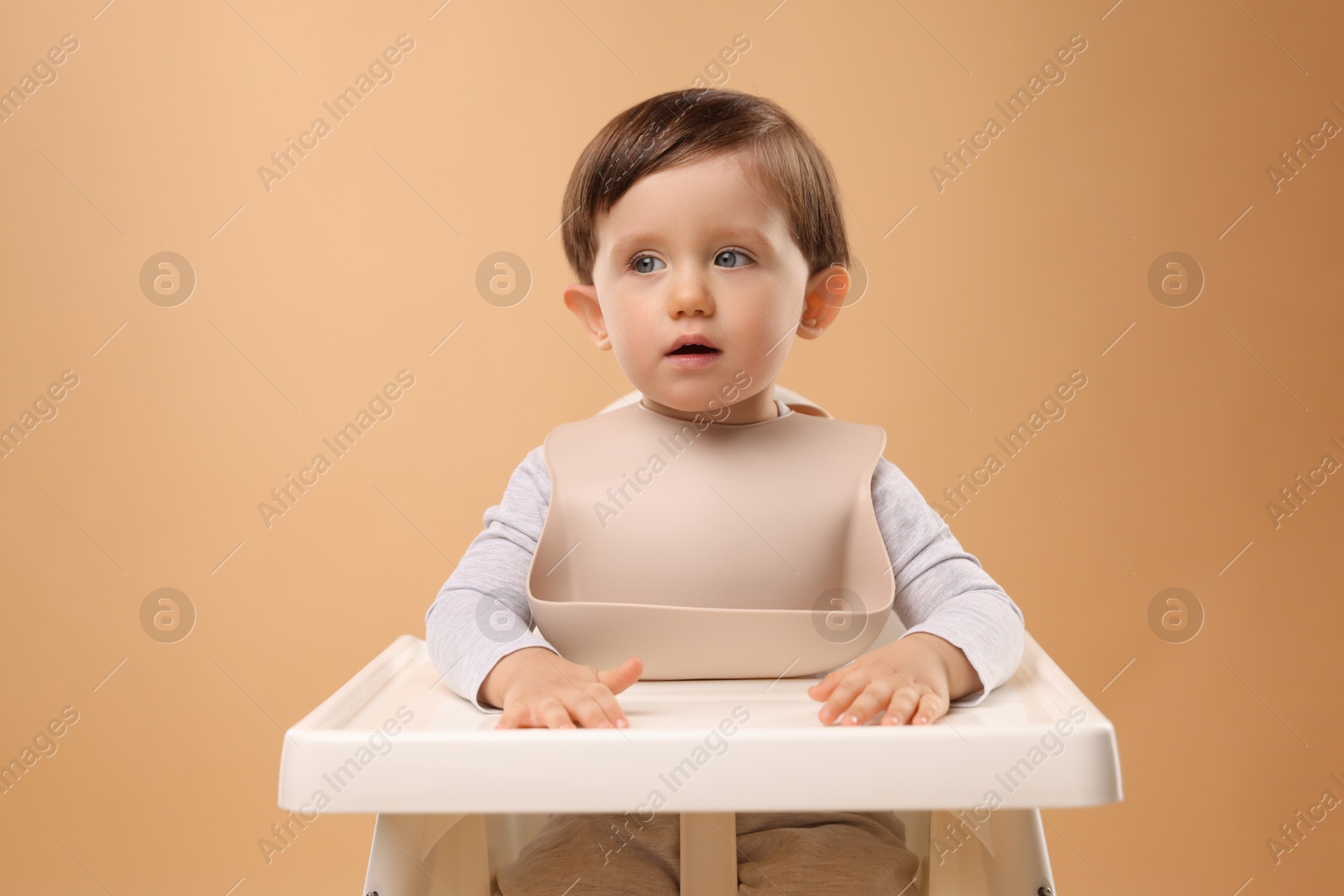 Photo of Cute little kid sitting in high chair on beige background