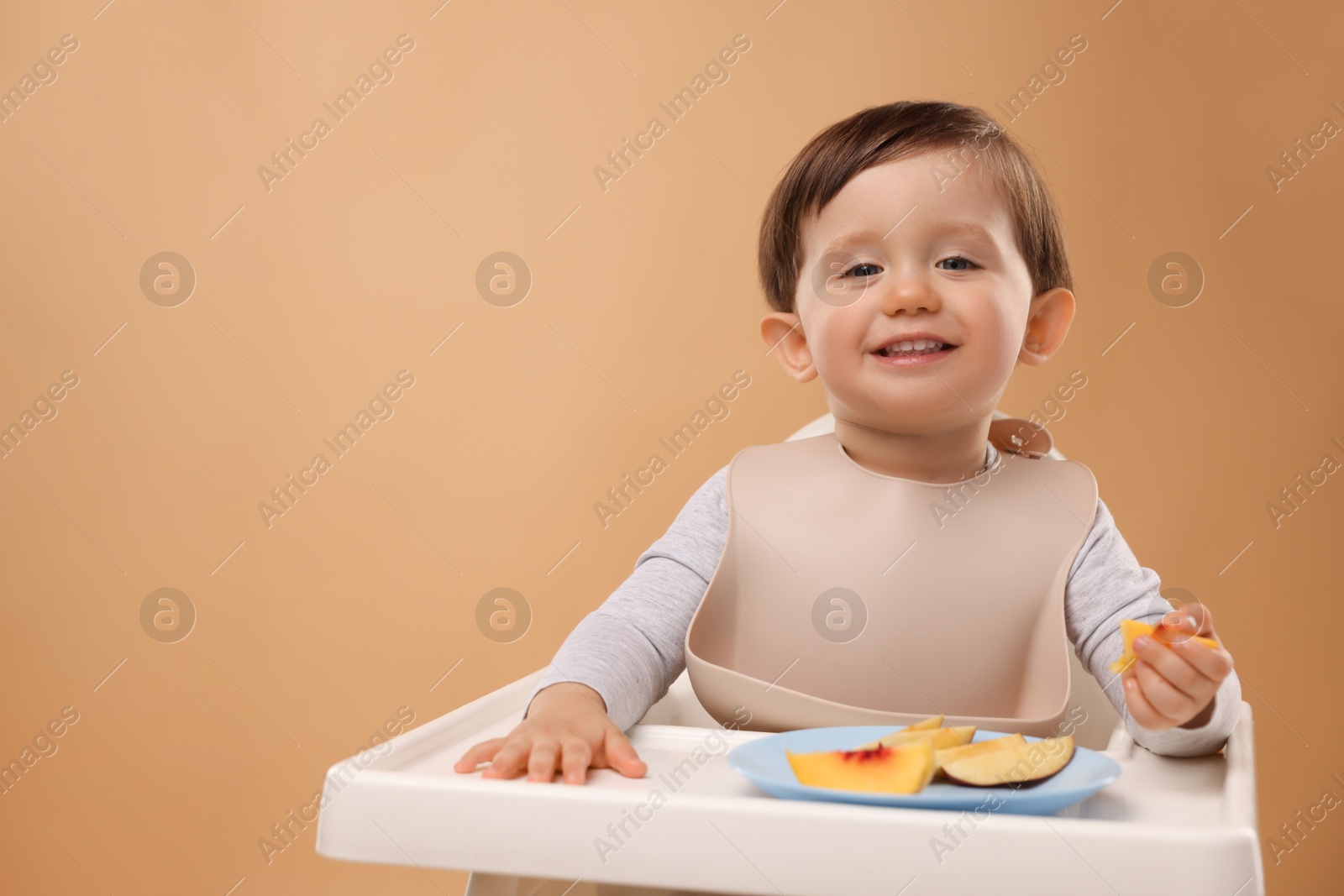 Photo of Healthy baby food. Cute little kid eating fruits in high chair on beige background, space for text