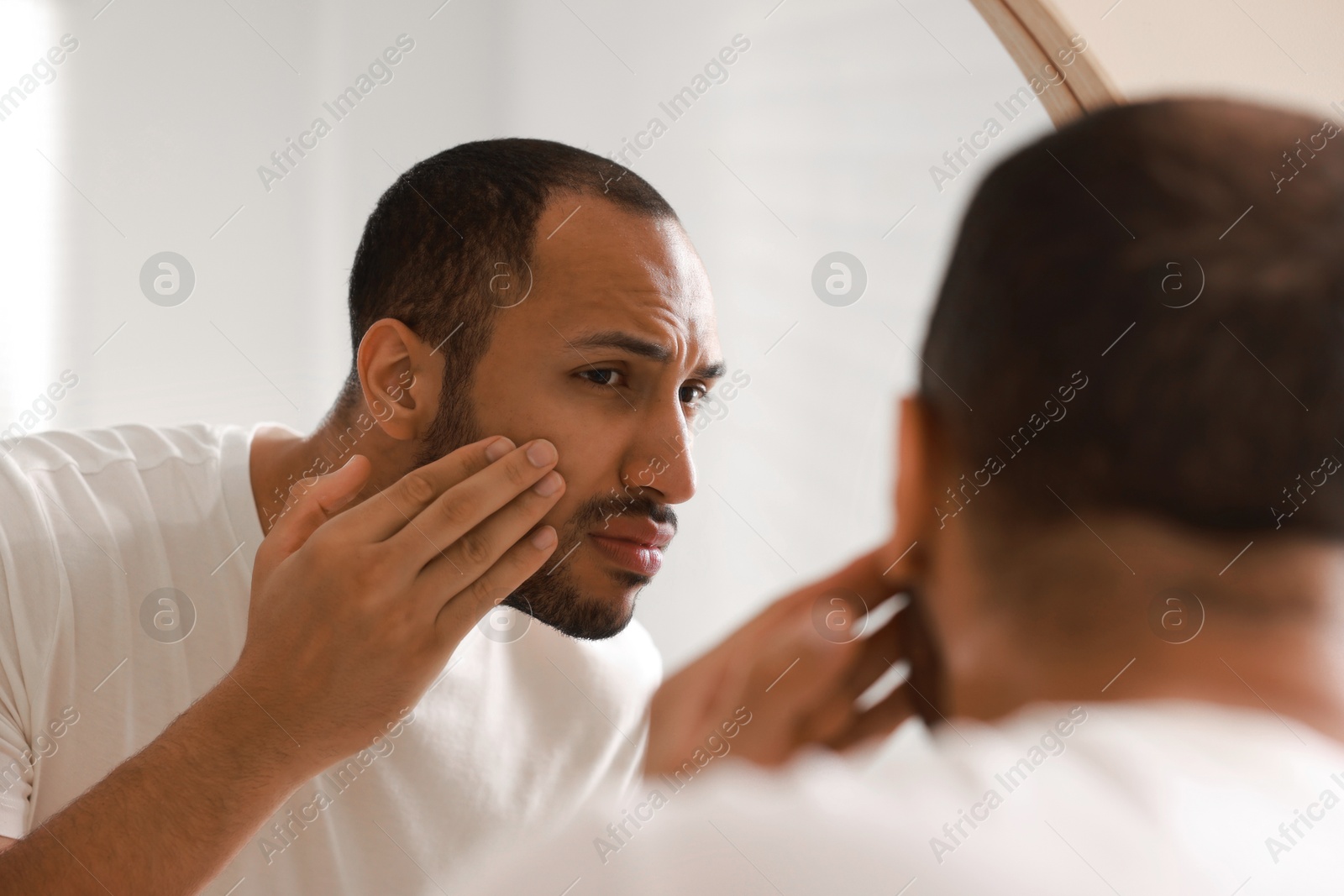 Photo of Worried man looking at mirror in bathroom