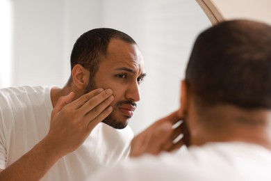 Photo of Worried man looking at mirror in bathroom