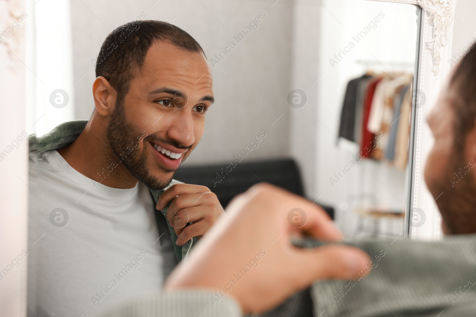 Photo of Smiling man dressing near mirror at home