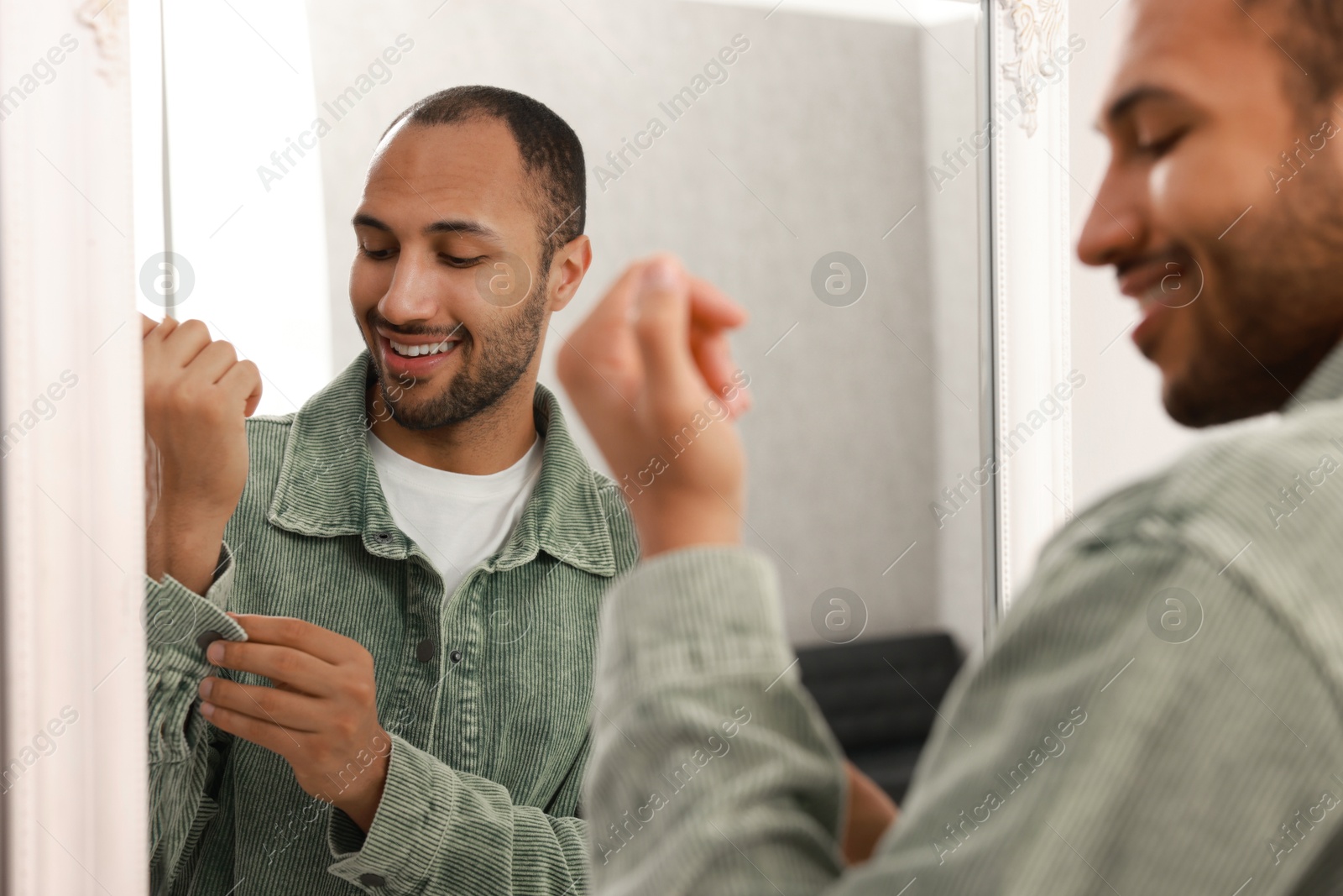 Photo of Smiling man dressing near mirror at home