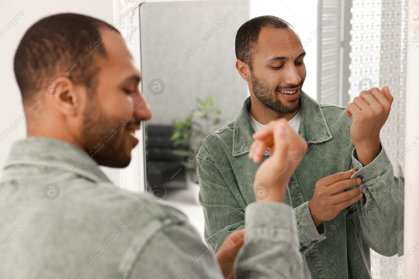 Photo of Smiling man dressing near mirror at home