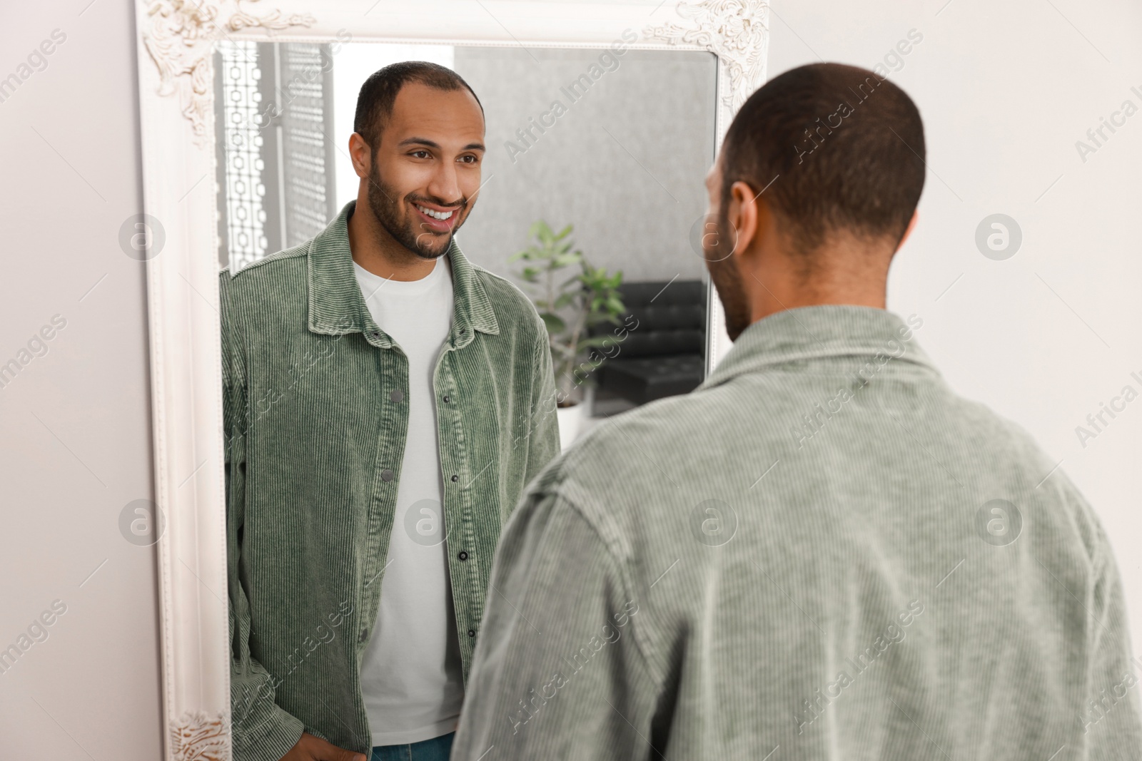 Photo of Smiling man looking at mirror at home, back view