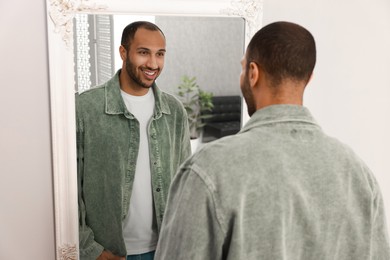 Smiling man looking at mirror at home, back view