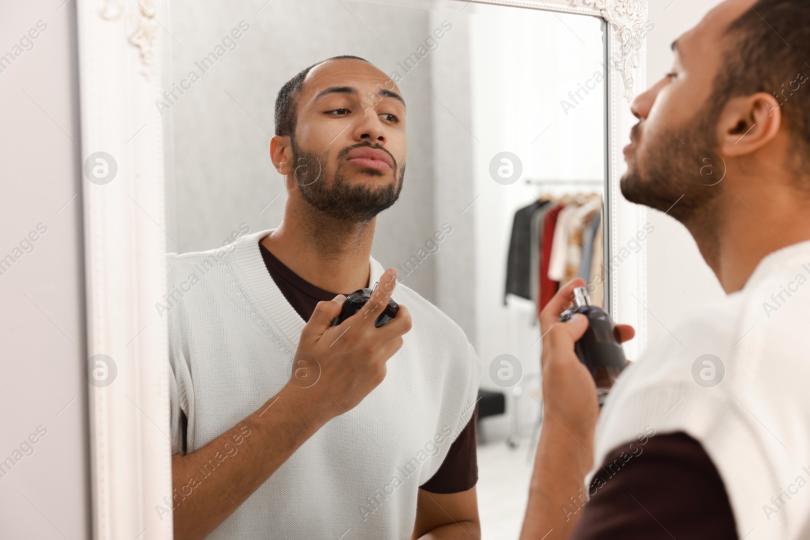 Photo of Handsome man spraying perfume near mirror at home