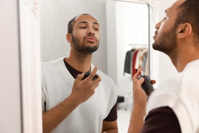 Photo of Handsome man spraying perfume near mirror at home