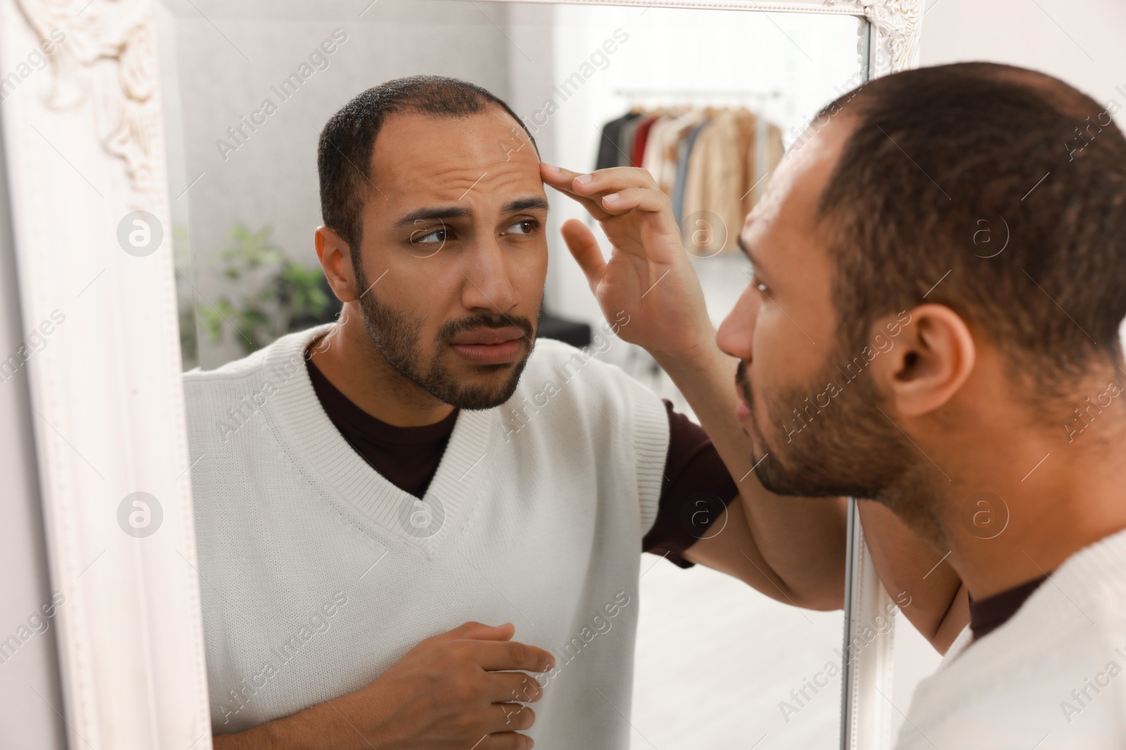 Photo of Worried man looking at mirror at home