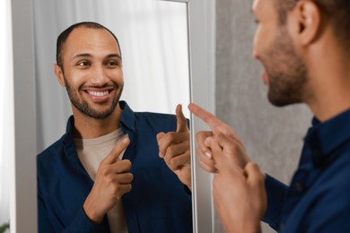 Photo of Smiling man looking at mirror at home