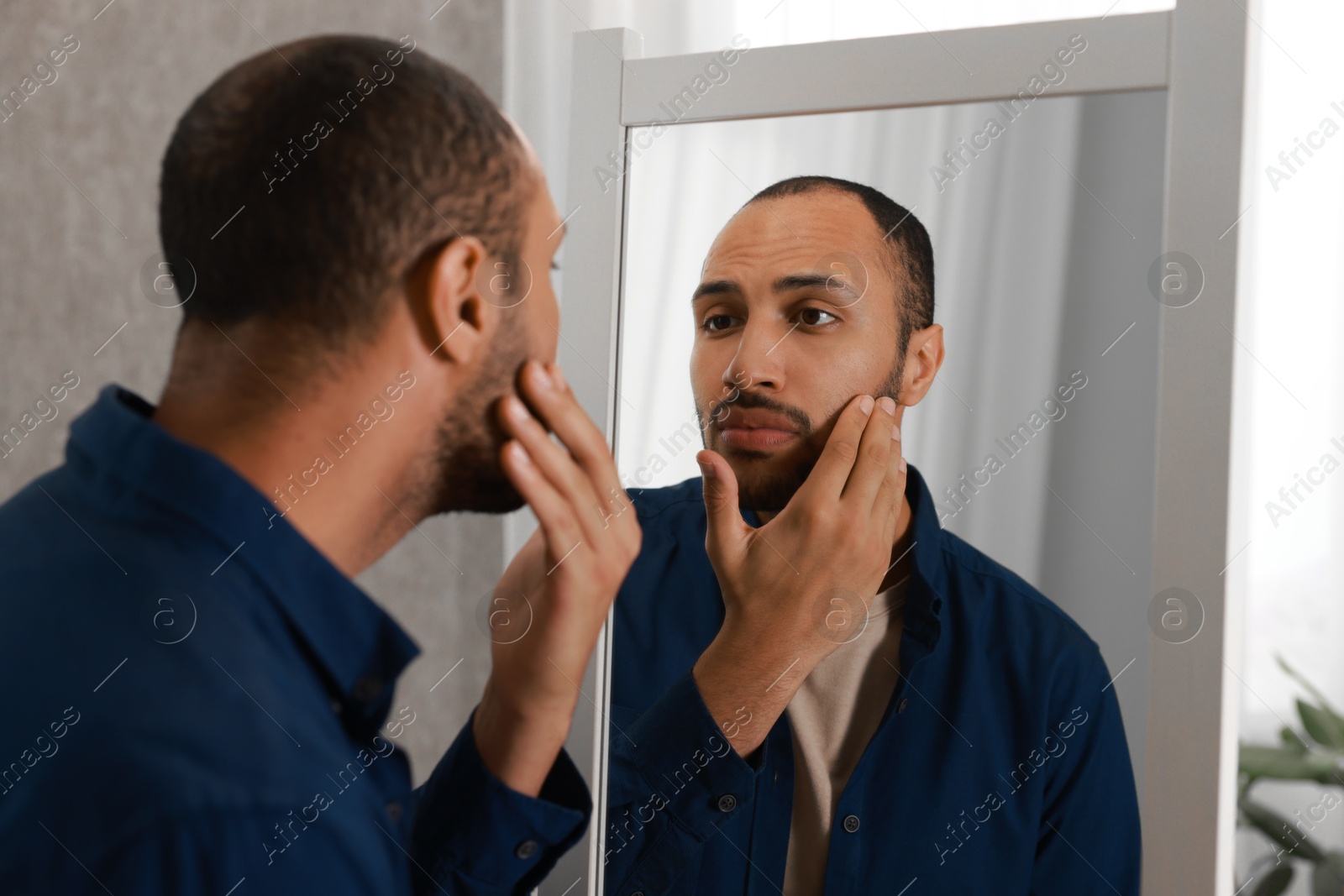 Photo of Worried man looking at mirror at home