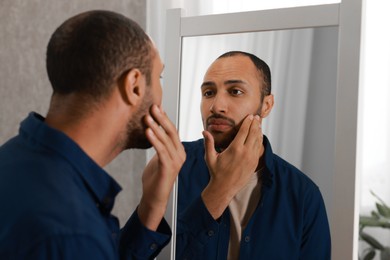 Worried man looking at mirror at home