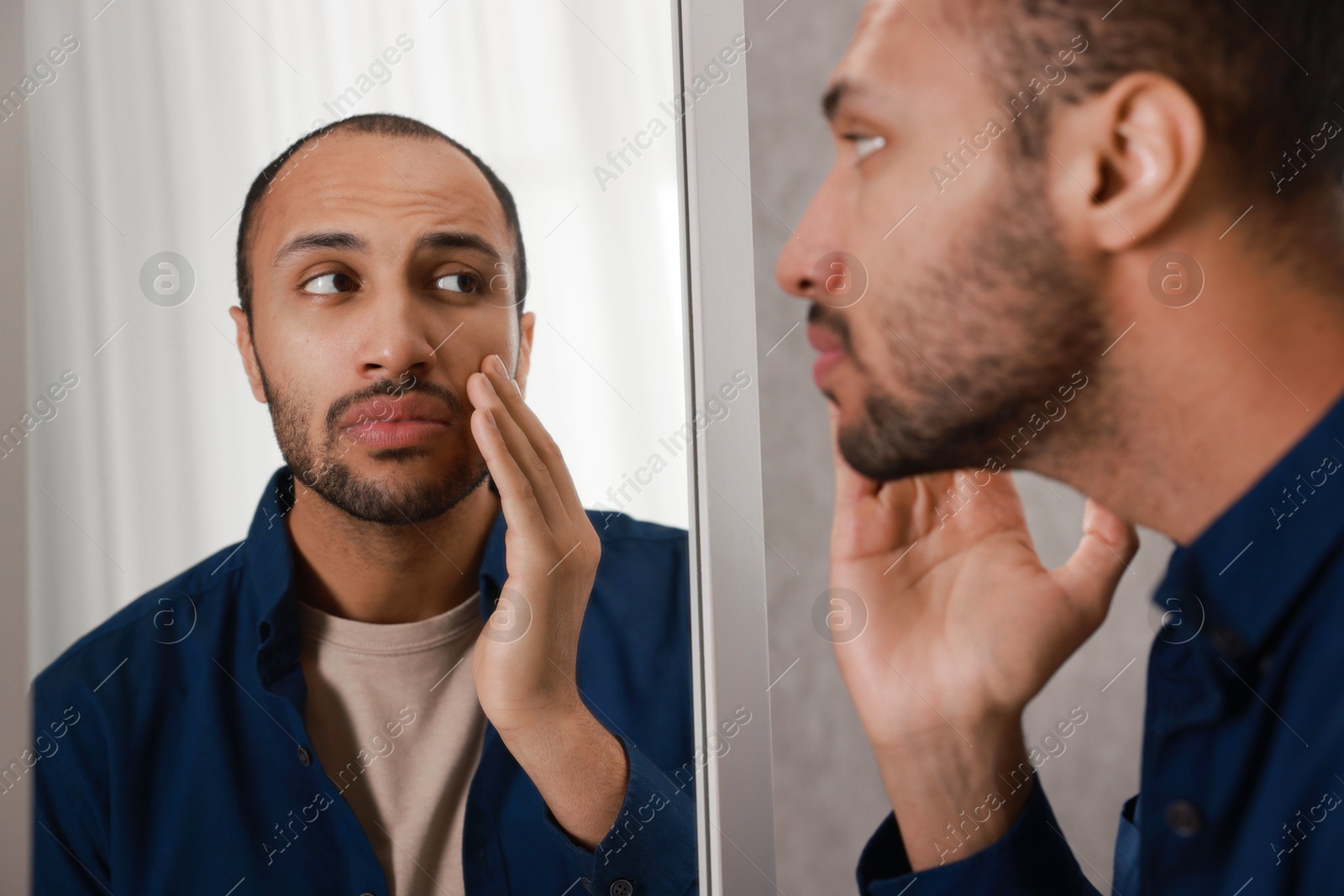 Photo of Worried man looking at mirror at home