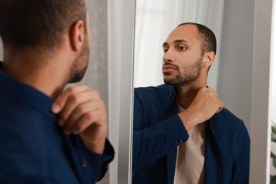 Worried man looking at mirror at home