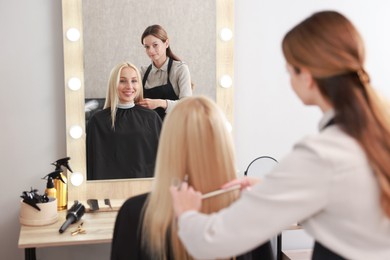 Photo of Professional hairdresser combing woman's hair in salon, selective focus