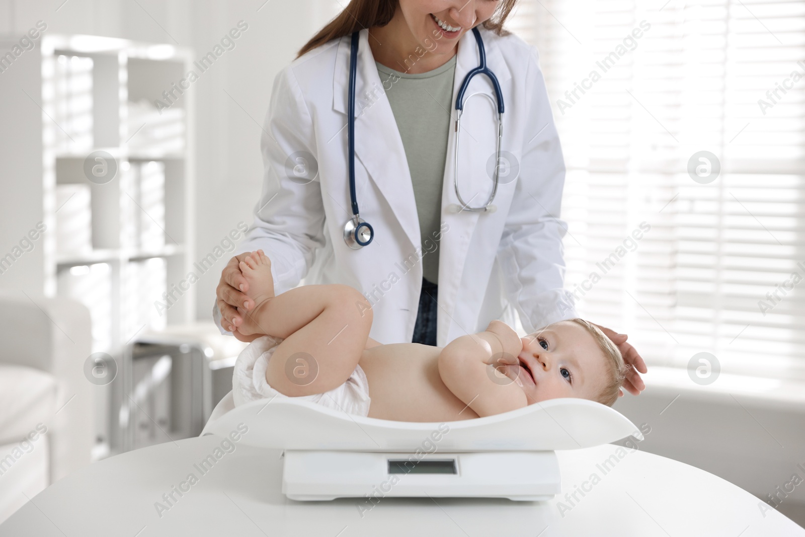 Photo of Pediatrician weighting little child in clinic, closeup. Checking baby's health