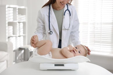 Pediatrician weighting little child in clinic, closeup. Checking baby's health