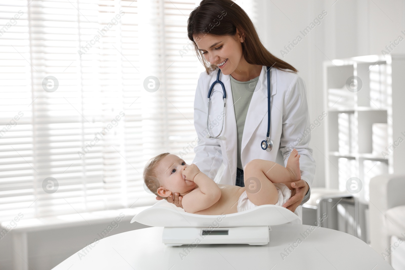 Photo of Pediatrician weighting little child in clinic. Checking baby's health