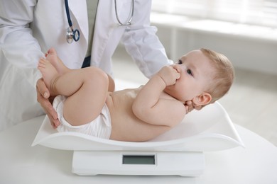 Photo of Pediatrician weighting little child in clinic, closeup. Checking baby's health