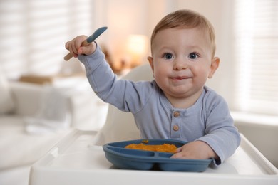 Cute little baby eating healthy food in high chair indoors