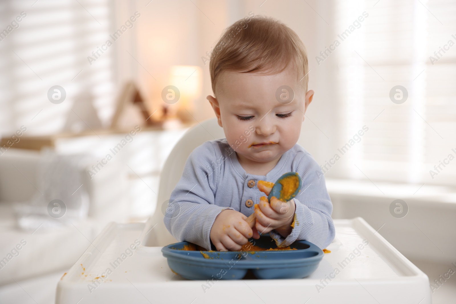 Photo of Cute little baby eating healthy food in high chair indoors