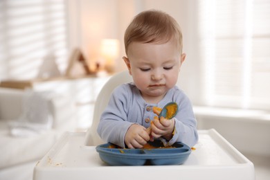 Photo of Cute little baby eating healthy food in high chair indoors