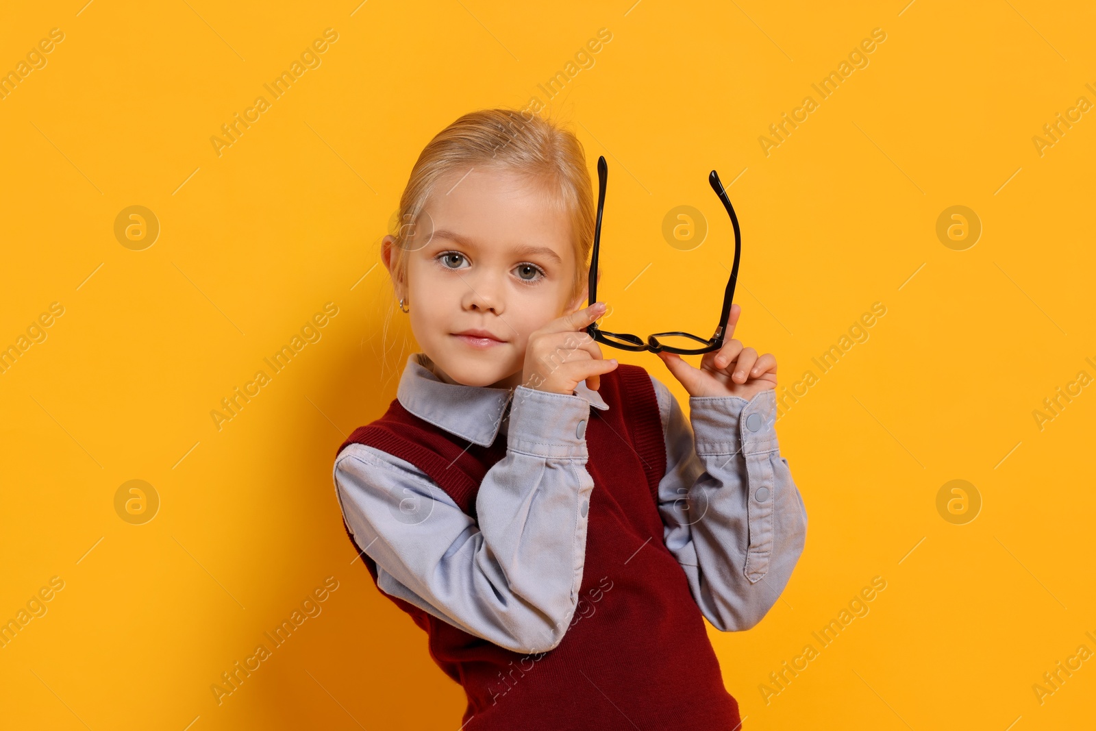 Photo of Little girl with glasses on orange background. Dreaming of future profession