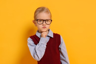 Photo of Little girl with glasses on orange background. Dreaming of future profession